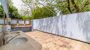 Un bagno esterno moderno con pavimento in legno, un lavandino grande e un pannello divisorio bianco.