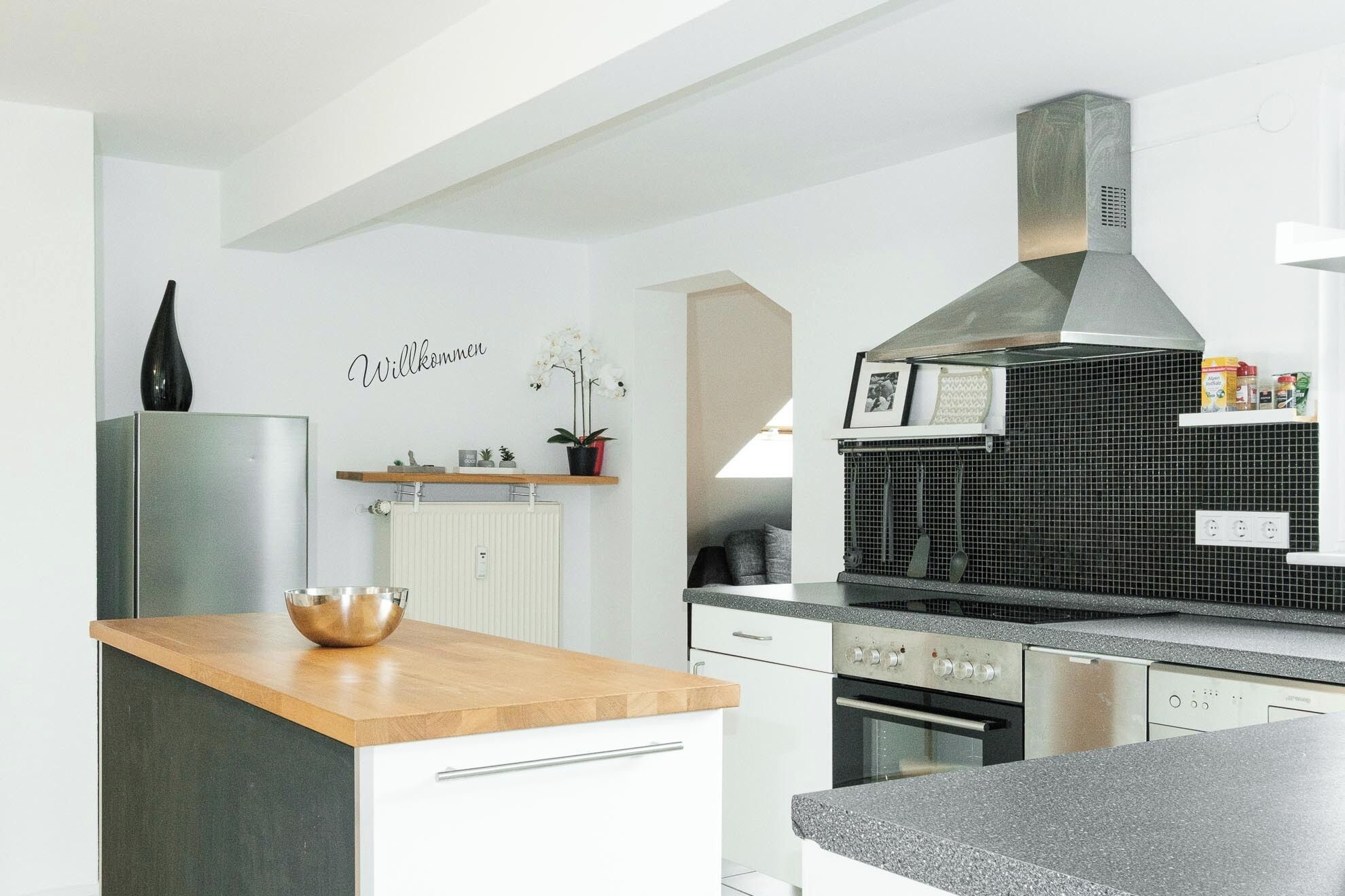 Una cocina moderna con armarios blancos, encimera de madera y campana extractora de acero inoxidable.
