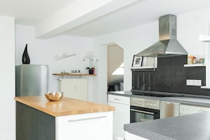 A modern kitchen with white cabinetry, a wooden countertop, and a stainless steel range hood. - Ferienwohnung mit Kuschelflair (Essen)