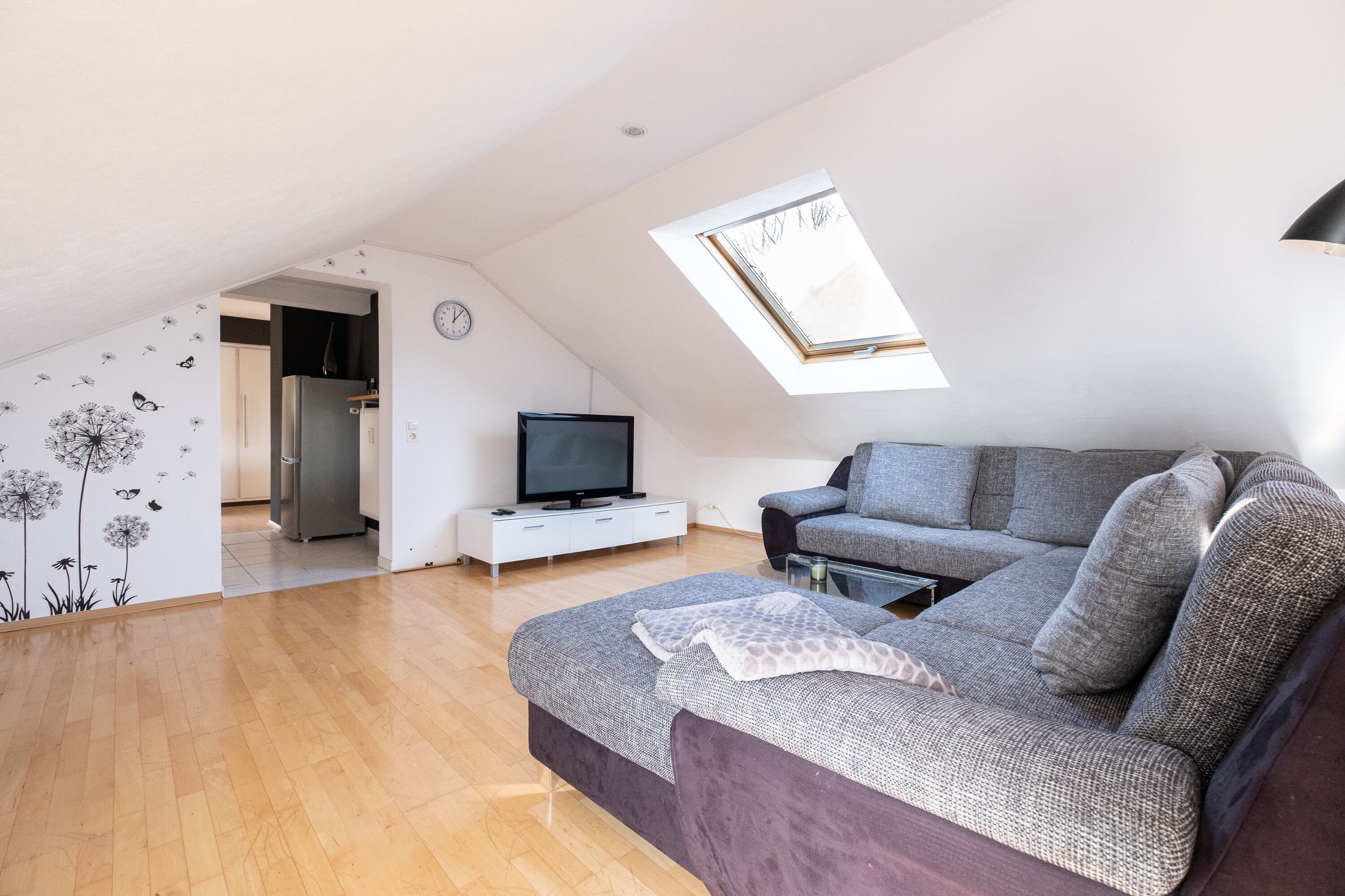 Una sala de estar moderna con techo estilo loft, un sofá gris, un televisor de pantalla plana y una mesa de comedor.