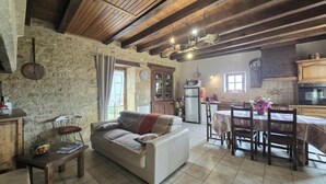 Un intérieur rustique avec des poutres apparentes, un mur en pierre, un canapé, une table à manger avec des chaises et un coin cuisine.
