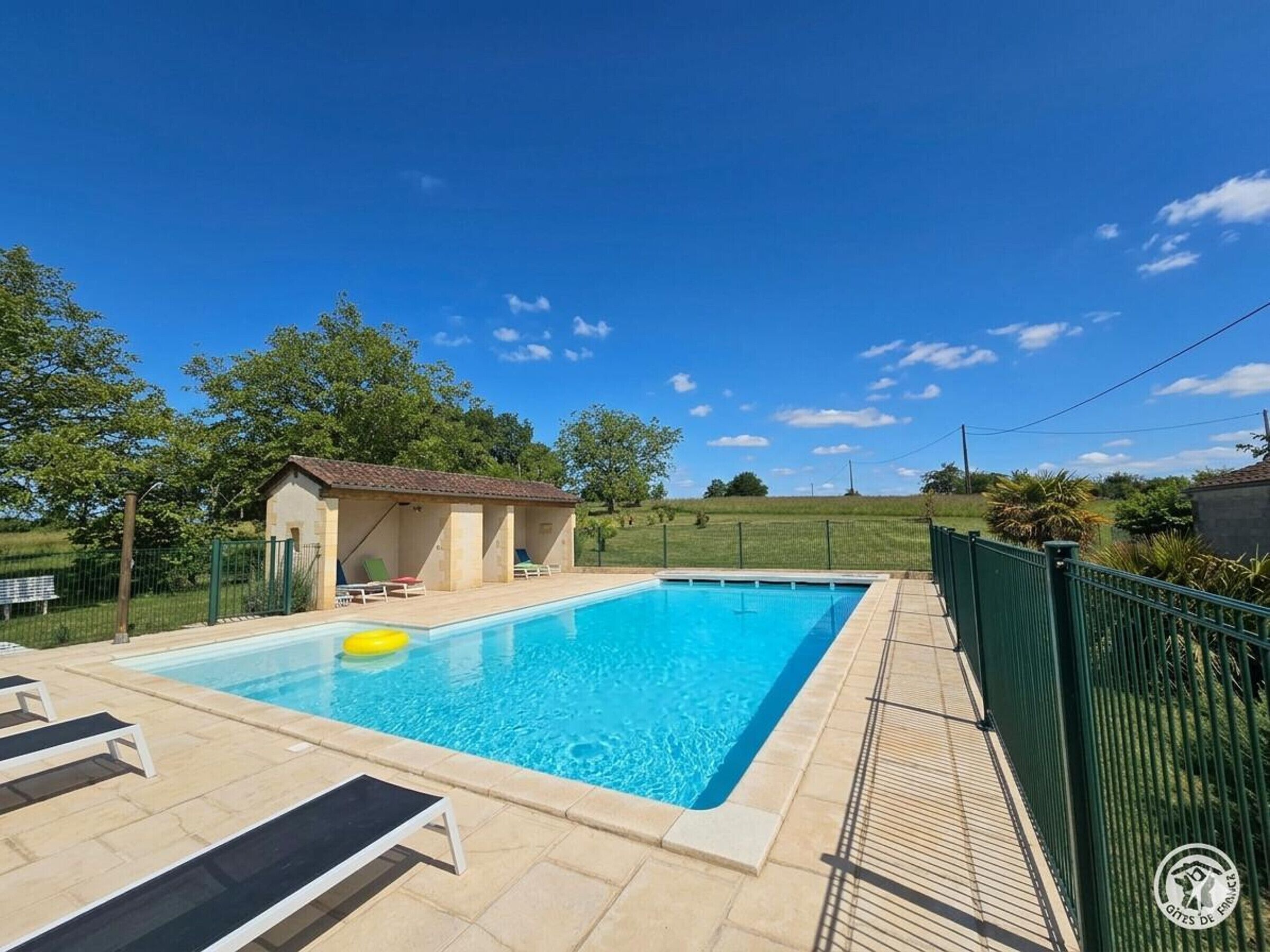 A swimming pool with lounge chairs, a small building, and a fenced area.