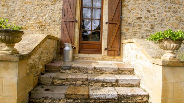 Un bâtiment en pierre avec une porte en bois, un seau en métal et des plantes en pot.