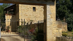 Un bâtiment en pierre avec un toit recouvert de tuiles, une petite fenêtre et un portail en métal.
