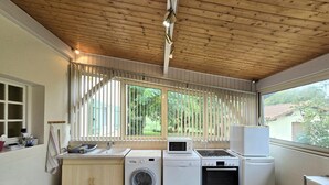 Cocina compacta con lavadora, microondas y horno, techo de madera y ventanas amplias con persianas.