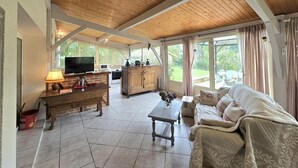 Un amplio salón con techo de madera, televisión, zona de cocina y sofá.