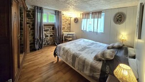 Un dormitorio con piso de madera, una cama con ropa de cama estampada, un escritorio y una pared de piedra.