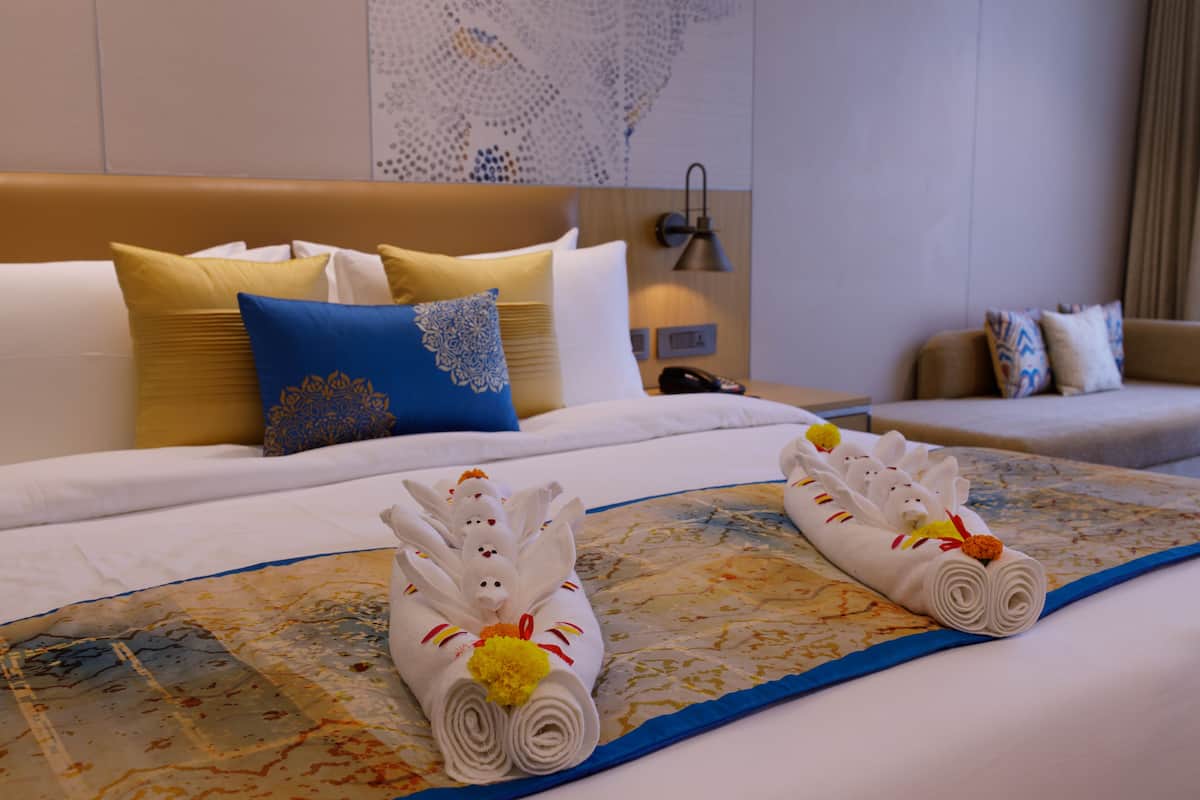 Une chambre d’hôtel avec un lit bien fait, un canapé et une table de chevet avec une lampe.