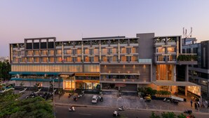 Un hotel de varios pisos con un diseño moderno, que cuenta con locales comerciales en la planta baja y habitaciones en el segundo piso.