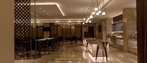 En modern hotellobby med ett blankpolerat marmorgolv, en receptionsdisk och en matplats med bord och stolar.