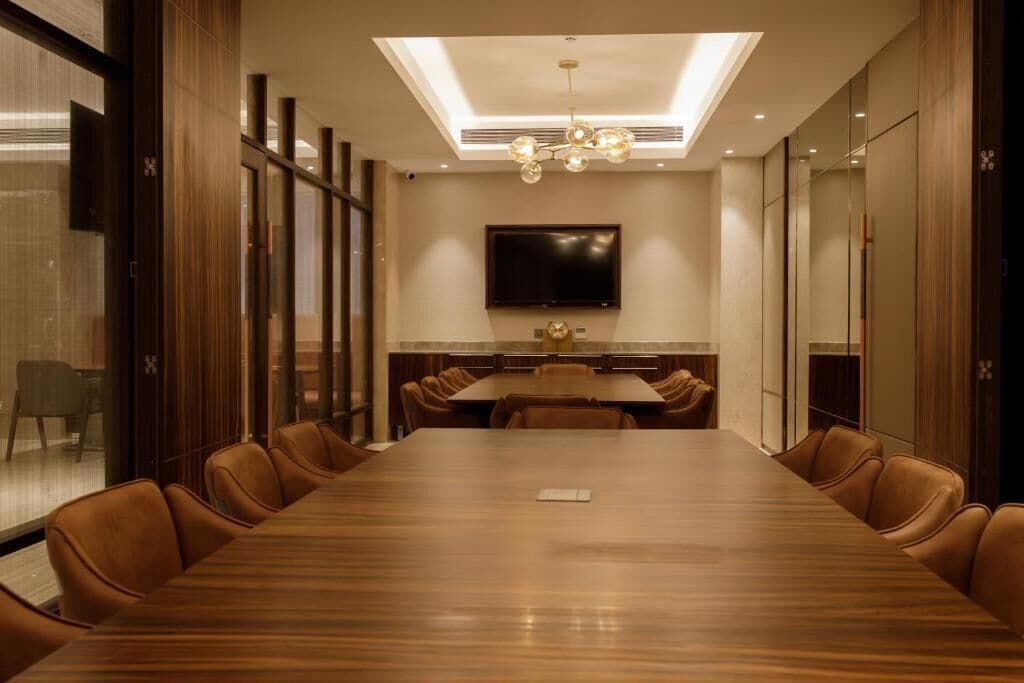 A conference room with a long table, leather chairs, a flat-screen TV, and a ceiling light fixture.