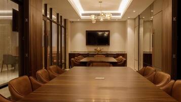 A conference room with a long table, leather chairs, a flat-screen TV, and a ceiling light fixture.