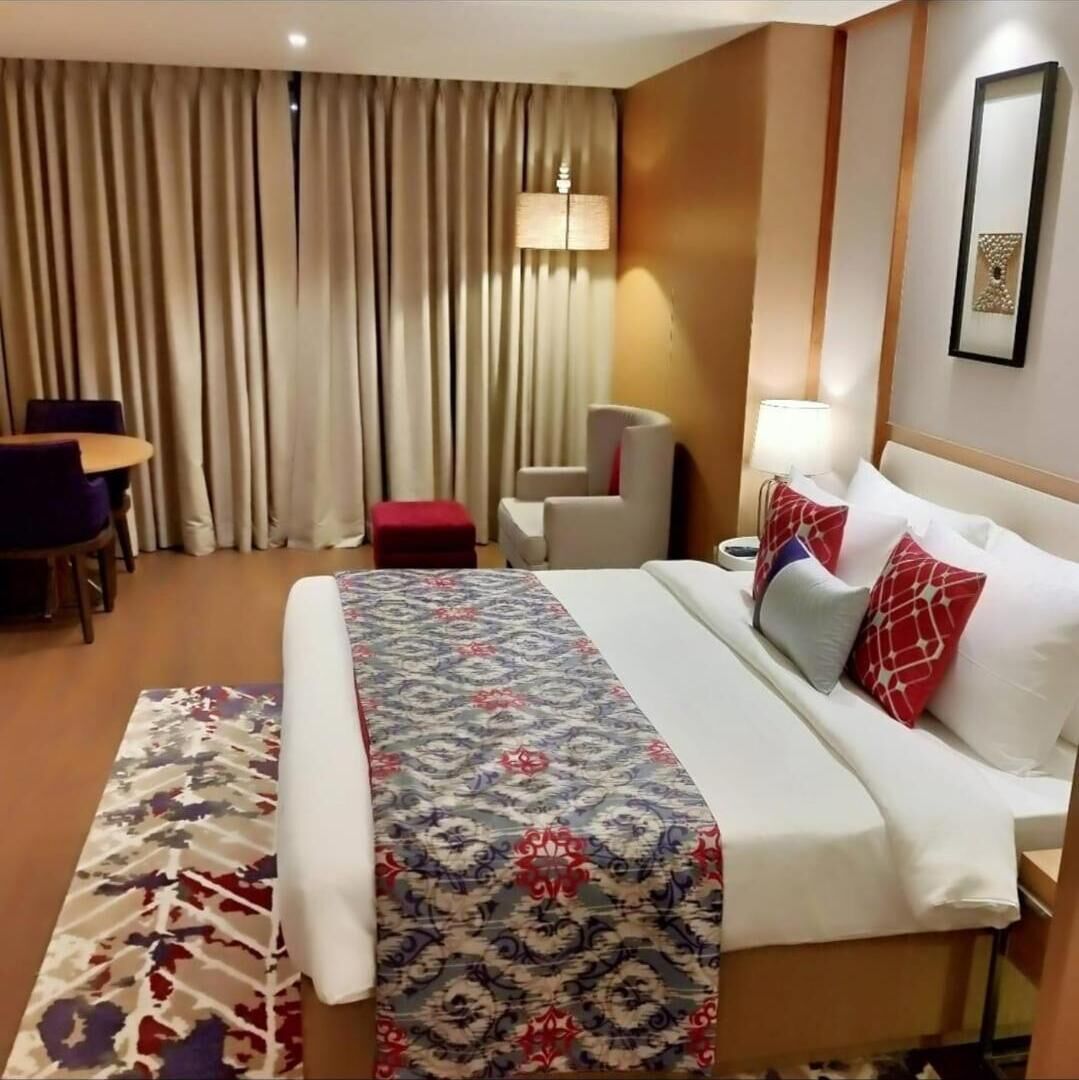 A hotel room with a bed, a desk, a chair, and a large window with curtains.