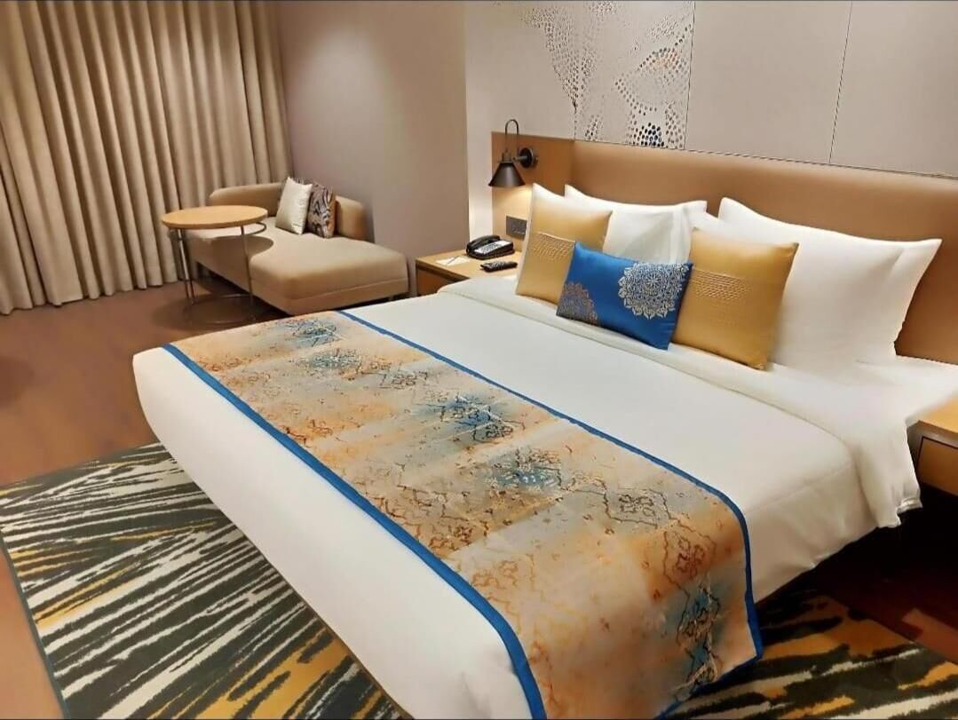 A hotel room with a bed, a nightstand, a bedside table, a sofa, and a patterned rug.