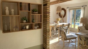 Een eethoek met een houten tafel en stoelen, een plank met decoratieve objecten, en uitzicht op de buitenwereld door een glazen deur.