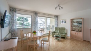 Ein Wohnzimmer mit Esstisch, Stühlen, einer Couch und einem Schrank mit dekorativen Tellern.