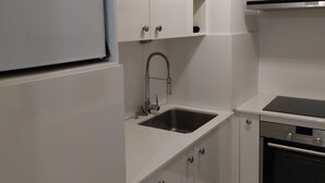 Eine moderne Küche mit weißen Schränken, einer Edelstahlspüle, einem Einbauofen und einem Kühlschrank.