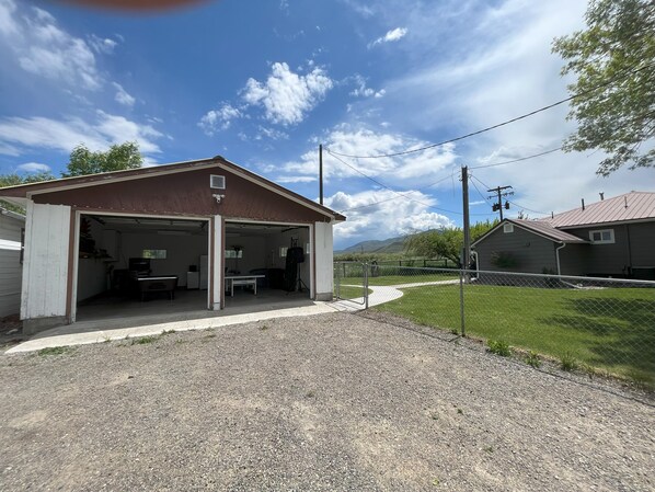 Eine Garage mit Überdachung, eine Auffahrt mit Kies, ein eingezäunter Garten und ein Haus im Hintergrund.