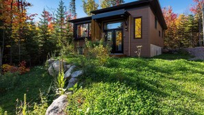 Eine moderne Hütte mit Glastür, umgeben von üppigem Garten und Herbstlaub.