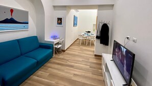 Ein modernes Wohnzimmer mit einem blauen Sofa, einem Fernseher und einem Essbereich mit Tisch und Stühlen.