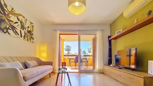 Ein modernes Wohnzimmer mit einer Couch, einem Glastisch, einem Flachbildfernseher und einem Balkon mit Gartenmöbeln.