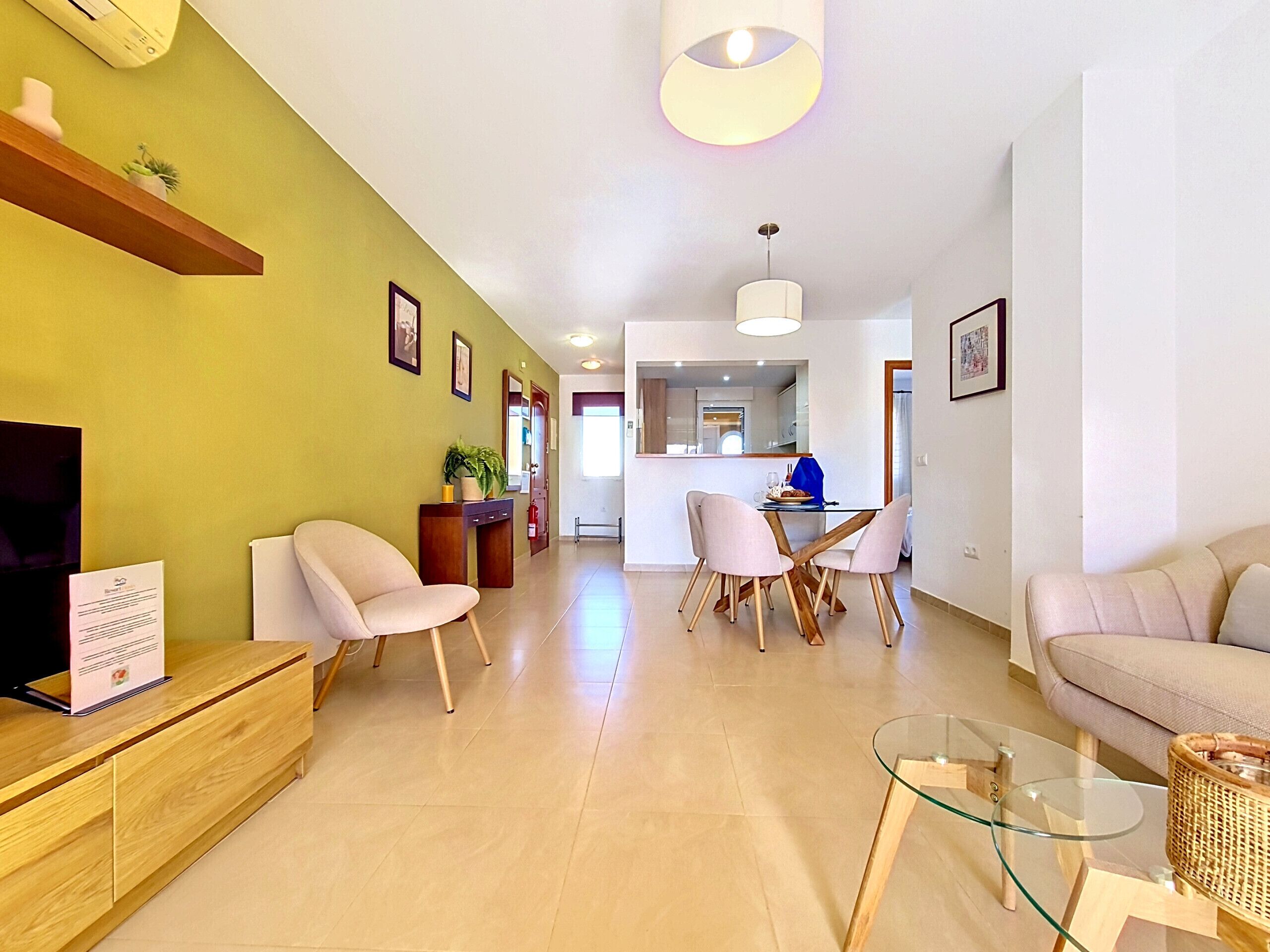 A modern living room with a sofa, chairs, a glass coffee table, a wooden side table, and a dining area with a table and chairs.