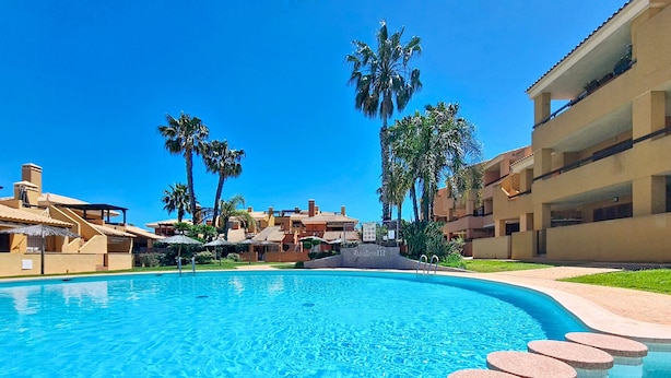 Ein Swimmingpool mit klarem, blauem Wasser, umgeben von Palmen und Hotelgebäuden.