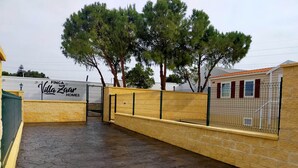 A gated parking area with a paved surface, a yellow fence, and a building with a sign reading "FINCA Villa Zaans Homes". - Mobile home 2 rooms (Puerto Real)