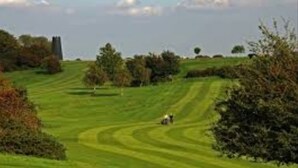 En golfbana med böljande, grönskande kullar, spridda träd och ett avlägset torn.