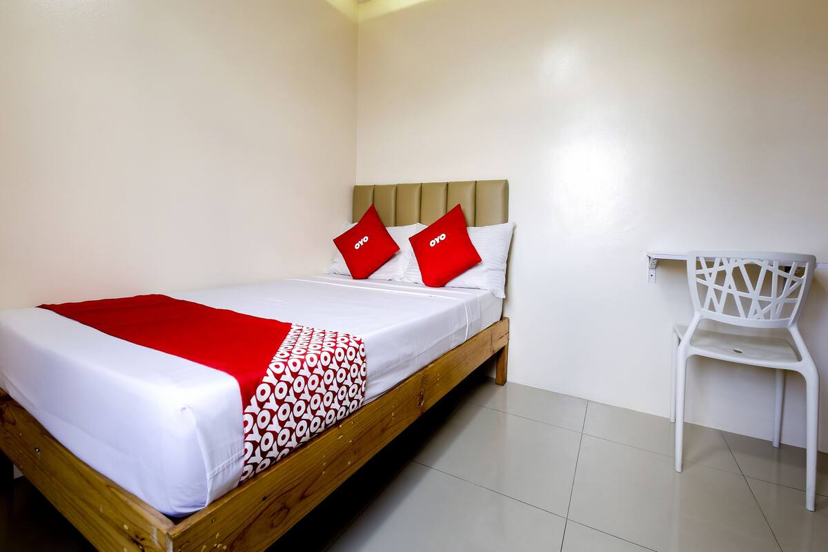A single bed with a wooden frame, white bedding, and red pillows with the logo "oyo".