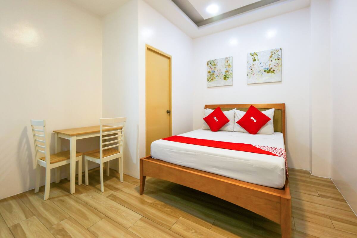 A bedroom with a wooden bed, white walls, a wooden desk, and two chairs.
