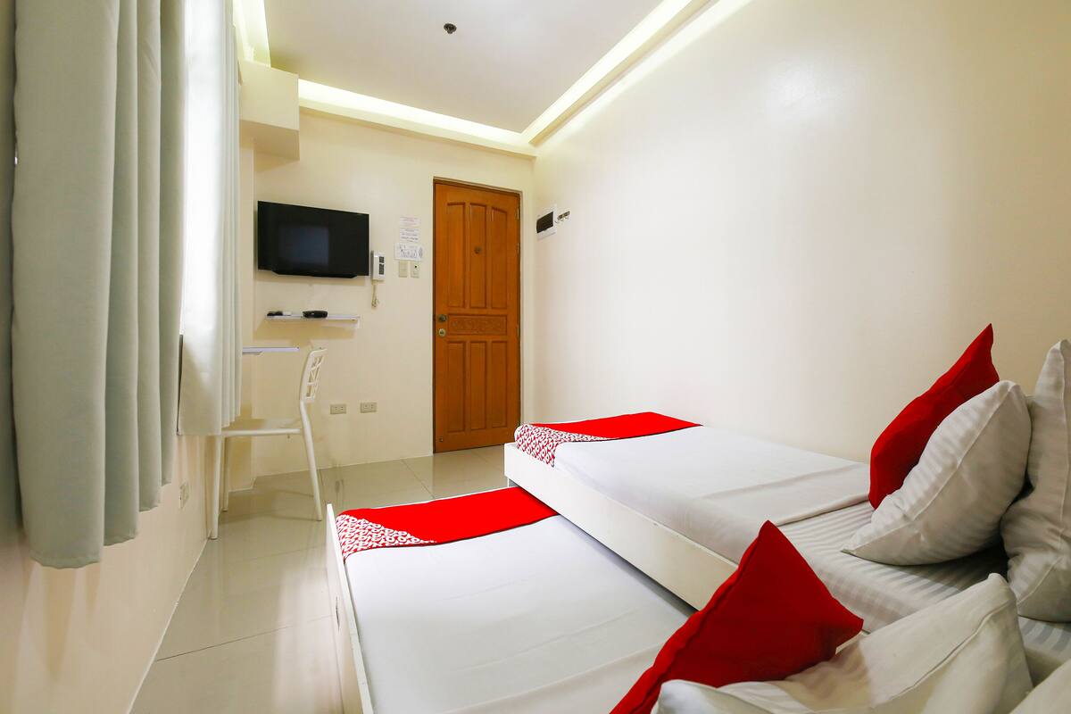 A hotel room with two beds, a TV mounted on the wall, a wooden door, and a white floor.