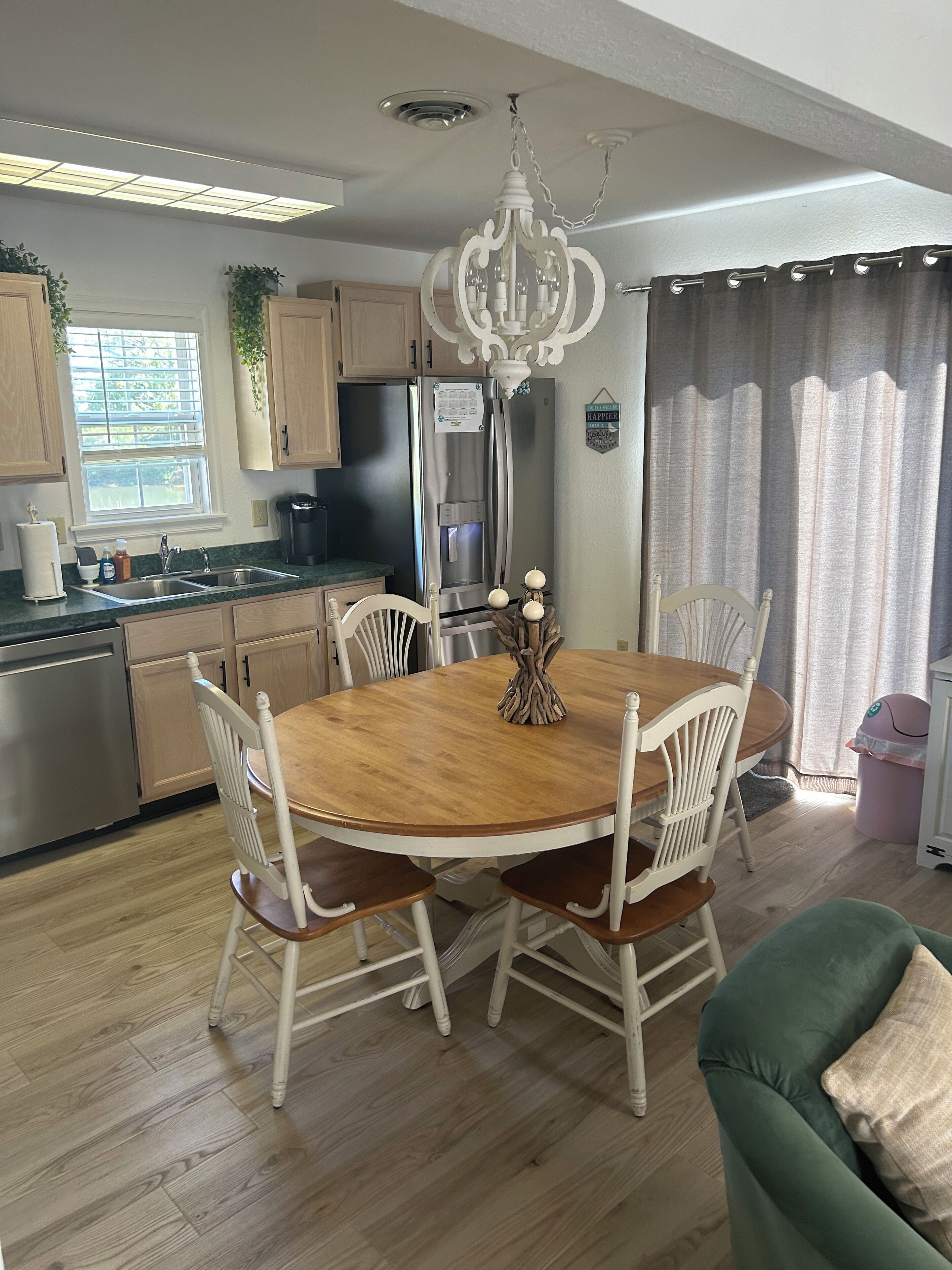 A dining area with a wooden table and white chairs, a chandelier, and a refrigerator.