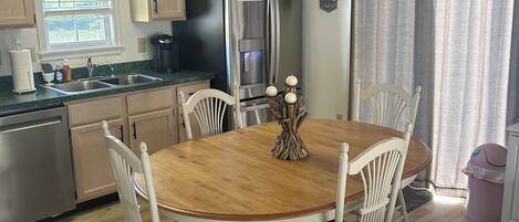 A dining area with a wooden table and white chairs, a chandelier, and a refrigerator.