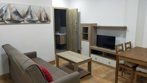 Olohuoneessa on sohva, sohvapöytä, televisio sekä ruokapöytä tuoleineen.