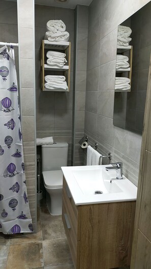 A bathroom with a toilet, sink, and shelves for towels. - 2-Bedroom Apartments (Puerto Real)