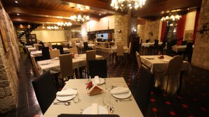 A restaurant with multiple dining tables set for guests, a stone wall, and a chandelier. - Llogora Tourist Village (Orikum)