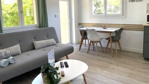 A modern living room with a grey sofa, a dining table with chairs, and a small kitchen area. - Auguière East, house in the heart of the vineyards (Hyères)