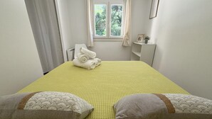A neatly made bed with a yellow textured bedspread, two pillows with a patterned design, and a window with curtains in the background. - Auguière East, house in the heart of the vineyards (Hyères)