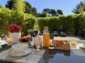 A breakfast table set outdoors with a variety of food items, a bottle of juice, and a vase of flowers.