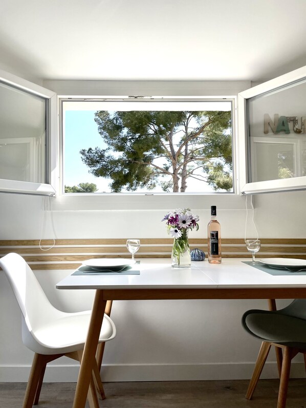 A dining area with a table set for two, a vase of flowers, and a bottle of liquor.