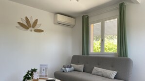 A modern living room with a grey sofa, a round white table, and a window with green curtains. - Auguière East, house in the heart of the vineyards (Hyères)