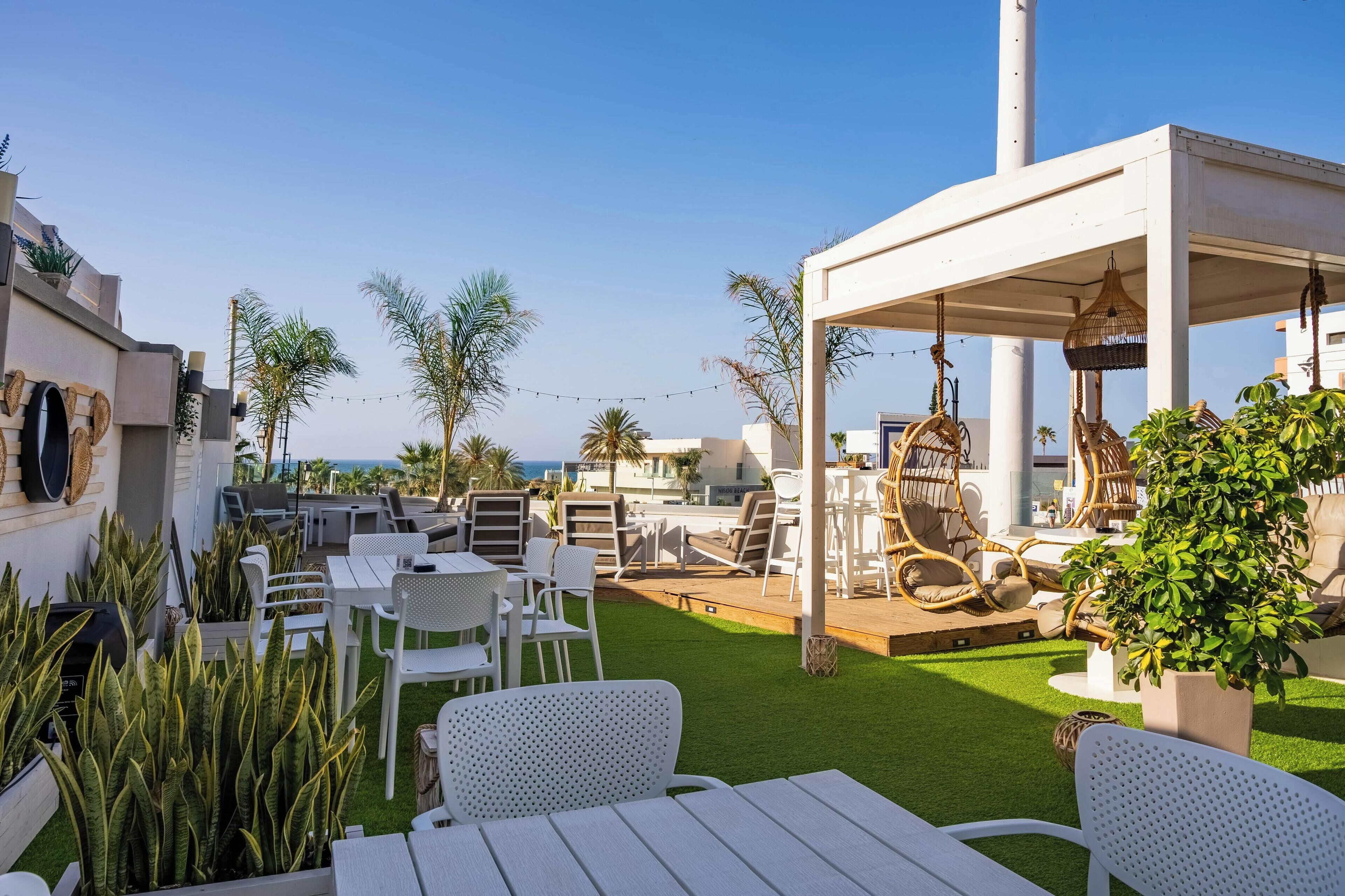 A rooftop terrace with white furniture, a pergola, and potted plants.