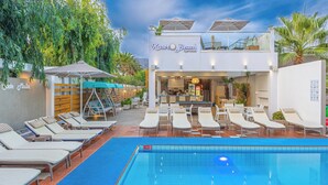 Een zwembadgedeelte met ligbedden en parasols, een restaurant en een bordje met Kaste Beach Apartments.