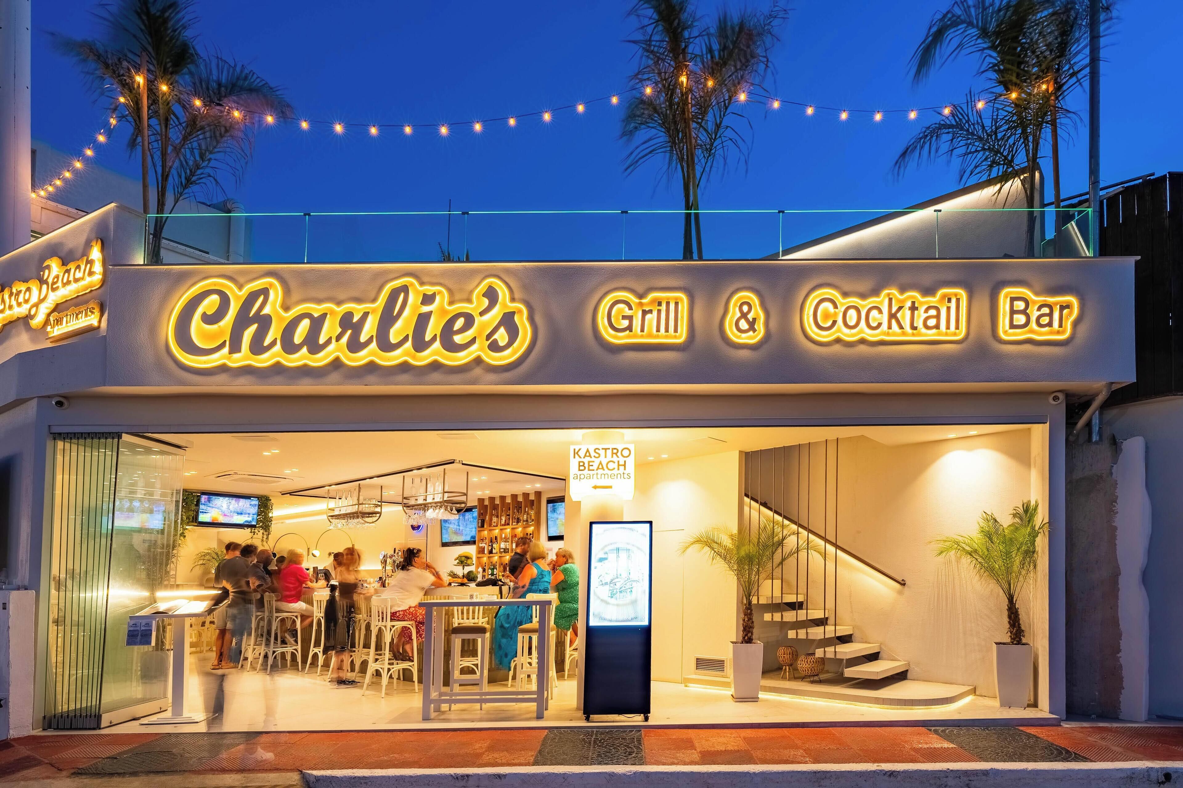 El restaurante y bar de cócteles Charlie's, con terraza y un cartel anunciando Apartamentos Kastro Beach.