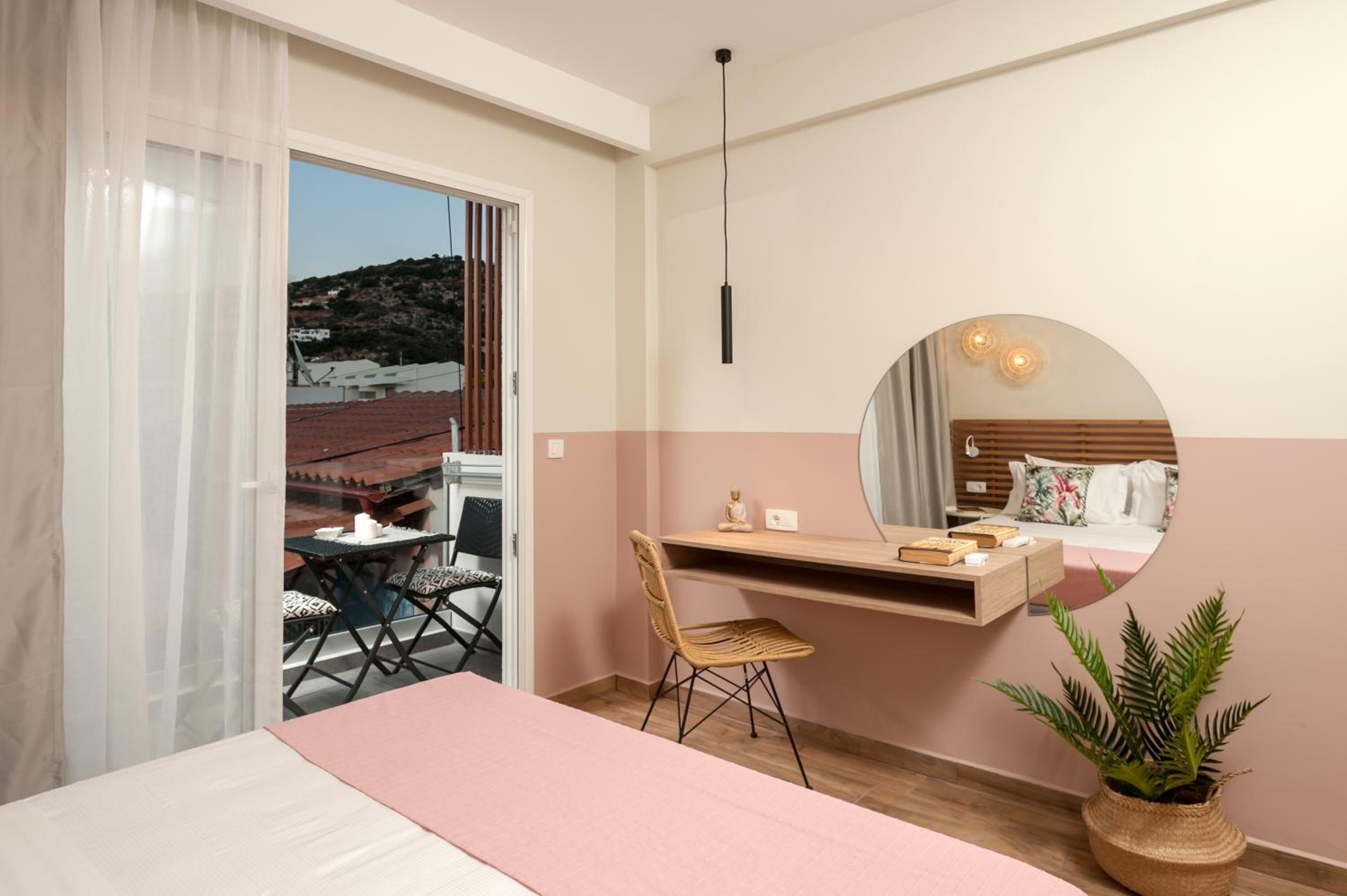 A bedroom with a bed, a desk, a chair, a mirror, and a potted plant.