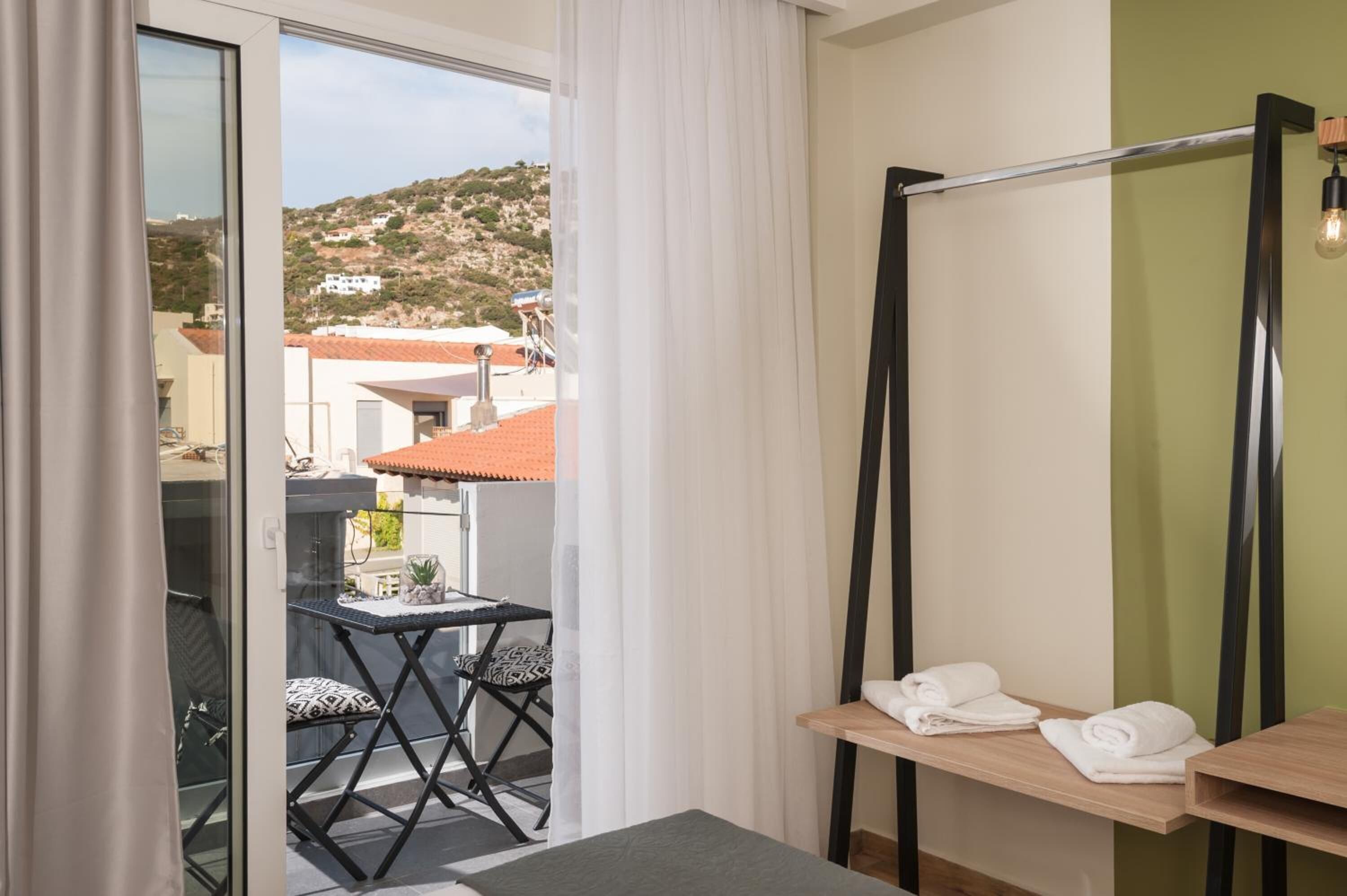 A balcony with a table and chairs, a view of buildings and hills, and a shower area with towels.