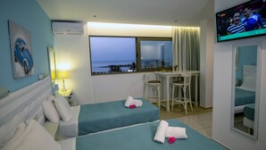 Een hotelkamer met twee bedden, een bureau, een televisie en een raam met uitzicht op zee.