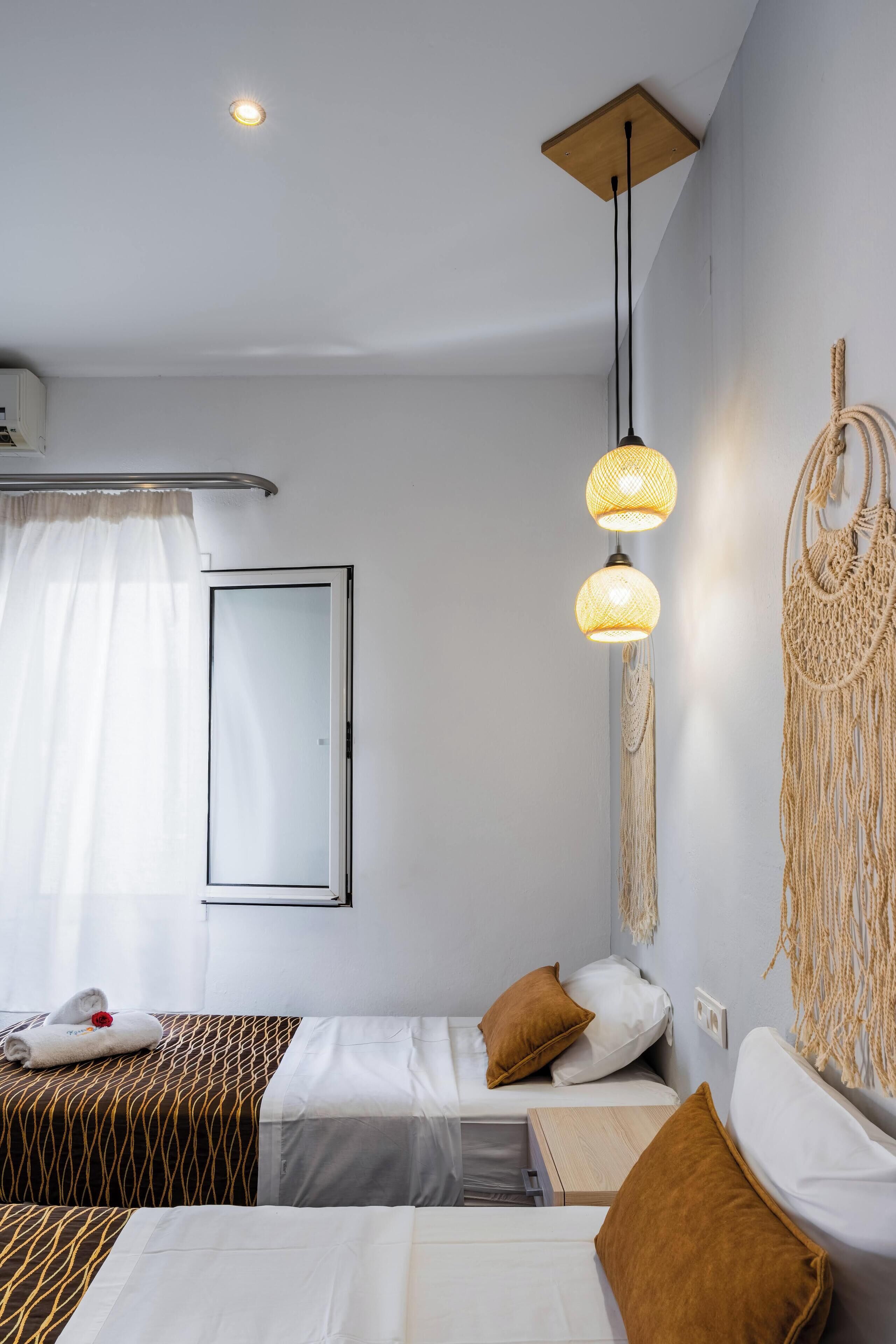 A hotel room with two beds, a mirror, a hanging macrame wall decoration, and a ceiling light fixture.
