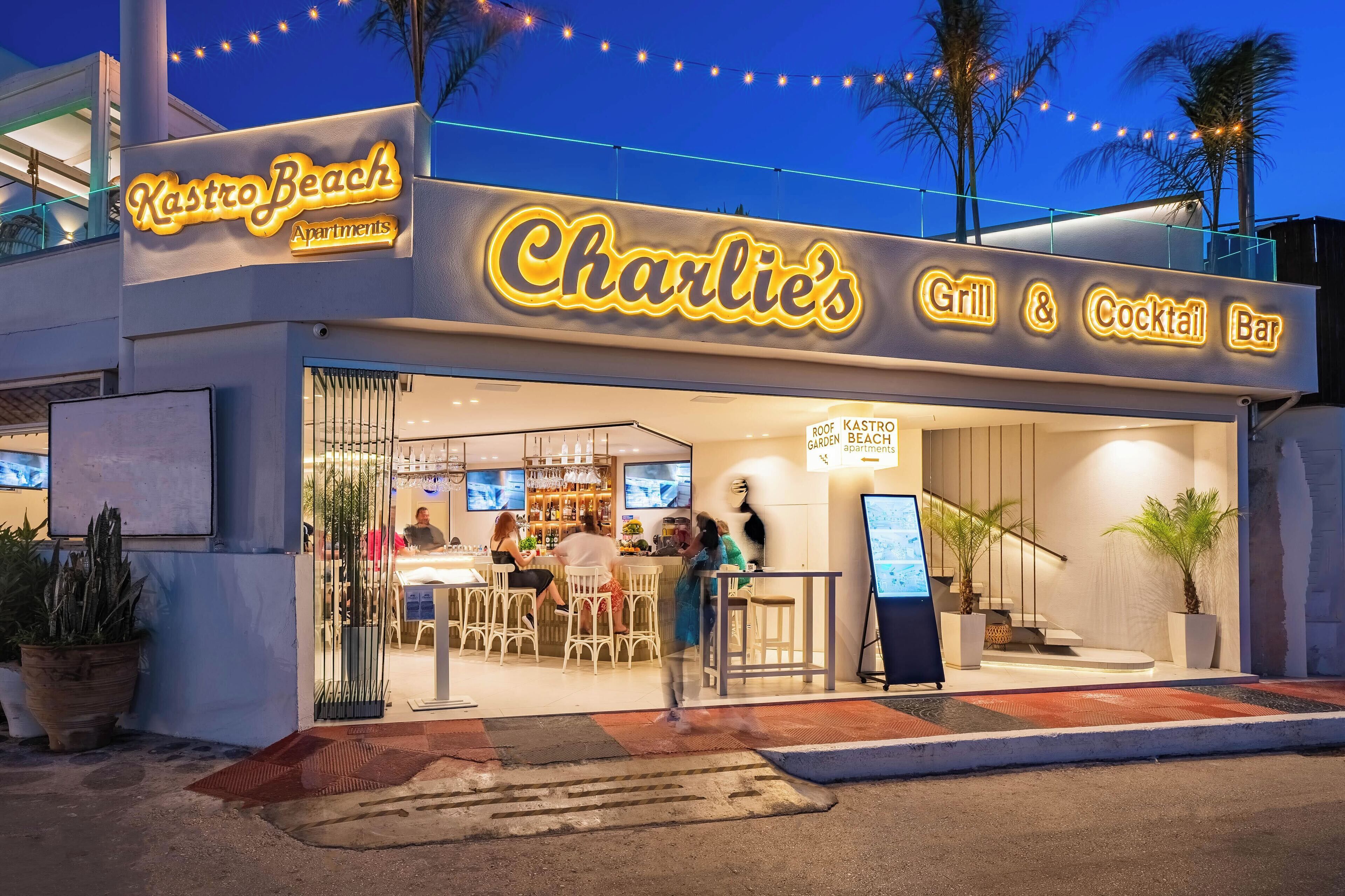 Charlie's Grill & Cocktail Bar med udendørs siddepladser og et skilt, der angiver, at det er en del af Kastro Beach Apartments.